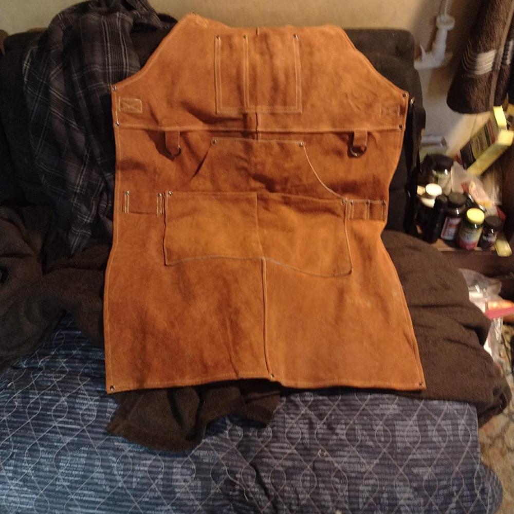 A brown split cowhide welding apron with a cross back strap and pockets